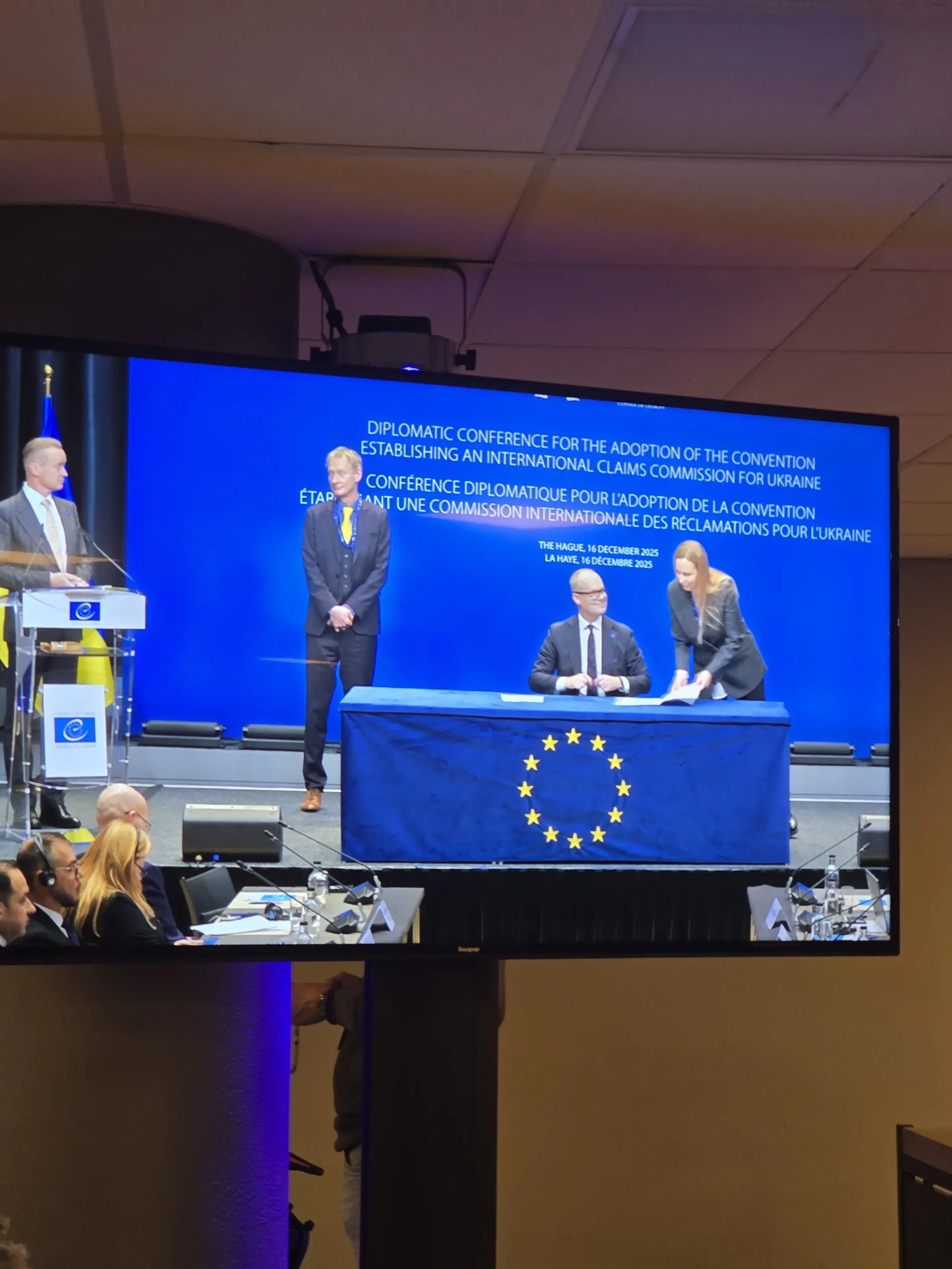 Large screen showing signing ceremony at Diplomatic Conference establishing International Claims Commission for Ukraine The Hague 2025